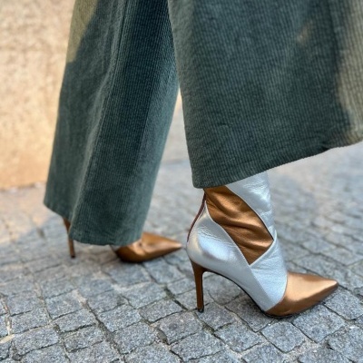 Botas de salto alto brancas e douradas com calças verdes num pavimento de calçada