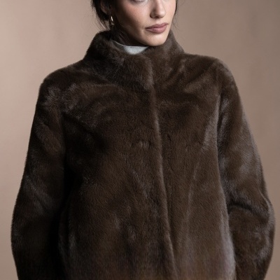 Mulher vestindo casaco de pele castanho escuro sobre camisola branca com gola alta