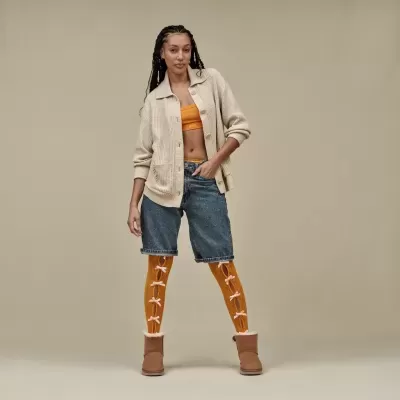 Mulher de cardigan bege, top laranja, calções ganga, meias laranja com laços e botas castanhas
