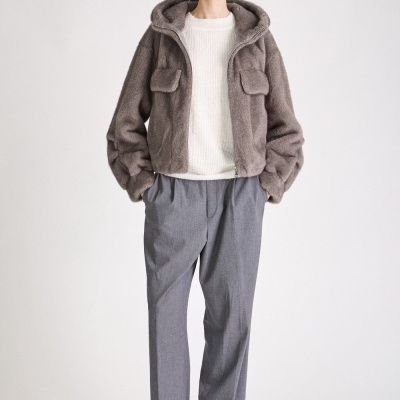 Mulher com casaco felpudo cinza, camisola branca, calças cinzentas e botas pretas em fundo branco