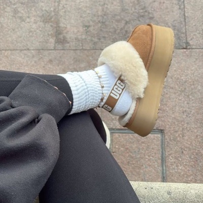 Sapato plataforma castanho claro com pêlo branco e meia UGG branca no pavimento de pedra