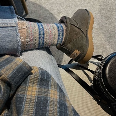 Botas UGG castanhas em camurça com meia colorida, calças de ganga e casaco aos quadrados.