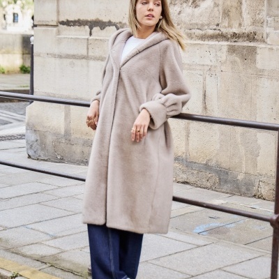 Mulher com casaco comprido bege claro, calças jeans azuis e ténis brancos na rua