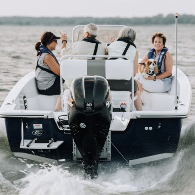 Barco de recreio azul escuro e branco com motor a navegar com quatro pessoas e um cão a bordo