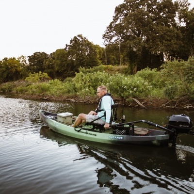 Homem em canoa verde com motor navegando num rio com vegetação