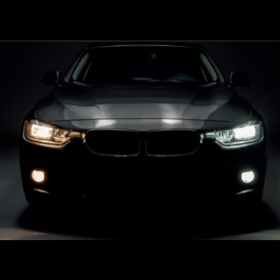 Frente de carro preto com faróis acesos num ambiente escuro