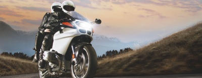 Motocicleta branca com dois motociclistas numa estrada de montanha ao pôr do sol