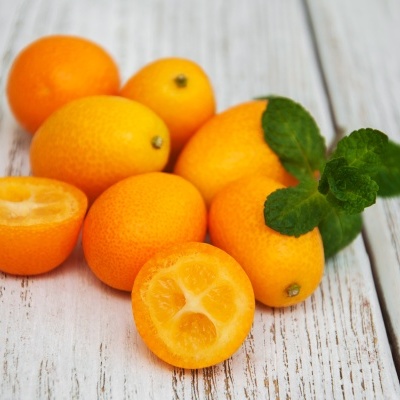 Frutos de kumquat laranja com folhas verdes sobre madeira branca envelhecida