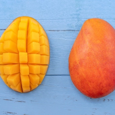 Duas mangas, uma inteira e outra cortada em cubos, sobre superfície azul.