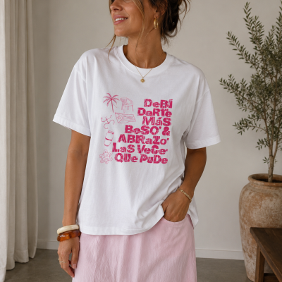 Mulher a usar t-shirt branca com texto rosa e saia rosa em interior com planta