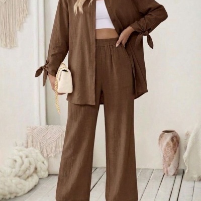 Conjunto castanho de camisa e calças largas com top branco e acessórios numa sala minimalista.