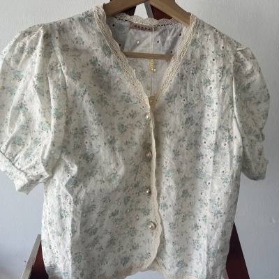 Blusa feminina branca com padrão floral azul e botões perolados