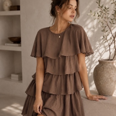 Vestido castanho com camadas em tecido leve usado por mulher em ambiente interior minimalista