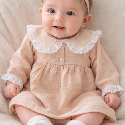 Bebé sentado com vestido bege e fita de cabelo com laço