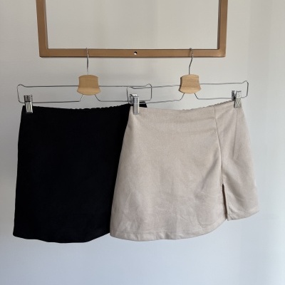 Duas saias curtas preta e bege penduradas em cabides de madeira e metal