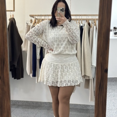 Vestido branco rendado com saia curta e botas douradas vistosos, mulher tira selfie em espelho de madeira.