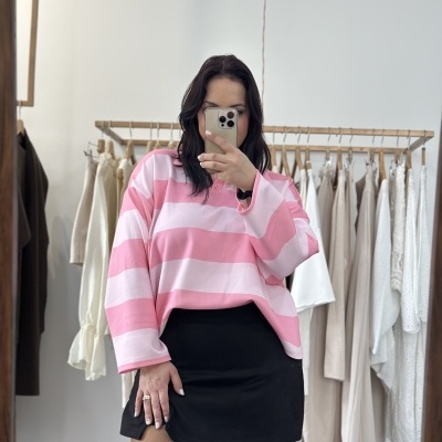 Pessoa vestindo camisola rosa e branca às riscas e saia preta em frente a cabide com roupas claras numa loja