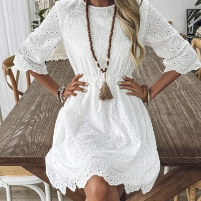 Vestido branco bordado com padrão floral, mangas 3/4, cintura franzida, colar de contas castanhas e chapéu de palha