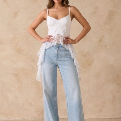Top branco com renda e calças de ganga largas azuis em fundo bege.