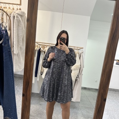 Mulher em espelho usando vestido curto preto com padrão prata e botas pretas com tachas