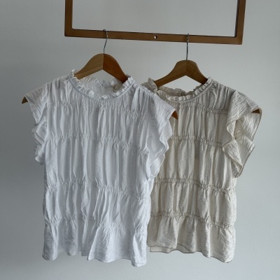 Duas blusas femininas leves com franzidos penduradas em cabides de madeira.