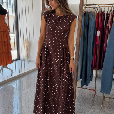 Vestido longo castanho com bolinhas brancas em mulher numa loja de roupa