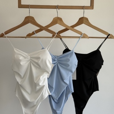 Três bodys com alças finas nas cores branco, azul claro e preto pendurados em cabides de madeira.