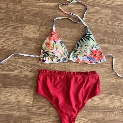 Biquíni com top floral colorido e cueca vermelha sobre piso de madeira.
