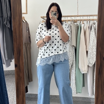 Mulher com t-shirt branca de bolinhas pretas, jeans azul claro e sandálias pretas com tiras em loja de roupa