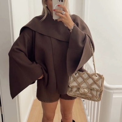 Mulher a usar casaco e shorts marrons com tachas, botas marrons e mala bege trançada com correntes douradas