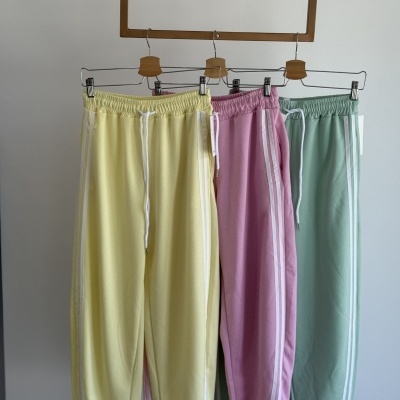 Três calças desportivas amarelo, rosa e verde com riscas brancas nas laterais penduradas