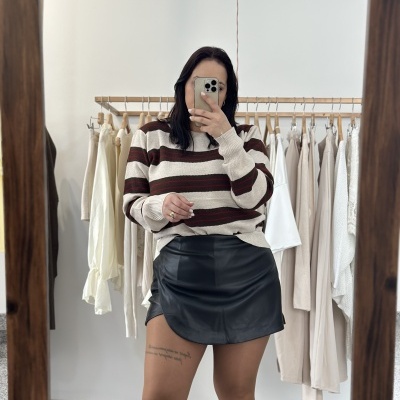 Mulher com camisola de malha riscada e saia preta em frente a cabide com roupas claras