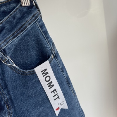 Jeans azuis com etiqueta MOM FIT pendurados num cabide metálico
