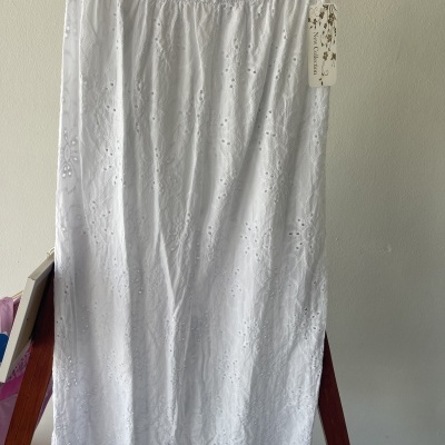 Saia branca bordada pendurada num cabide de madeira com etiqueta