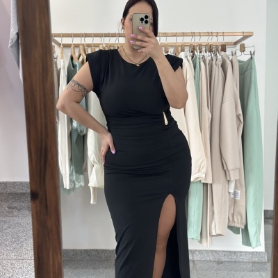 Vestido preto comprido com racha e fivela dourada, mulher a fazer selfie em espelho com roupa pendurada atrás