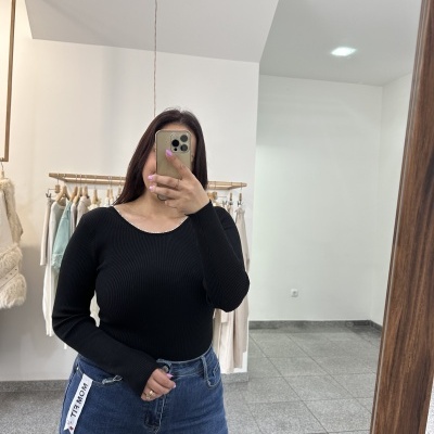 Mulher com camisola preta e calças de ganga mostra-se em espelho em loja de roupa.