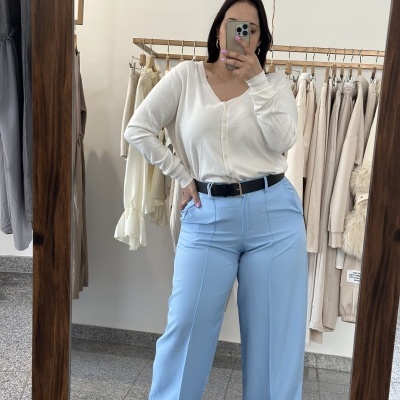 Pessoa com casaco branco e calças azuis em espelho, roupa pendurada ao fundo