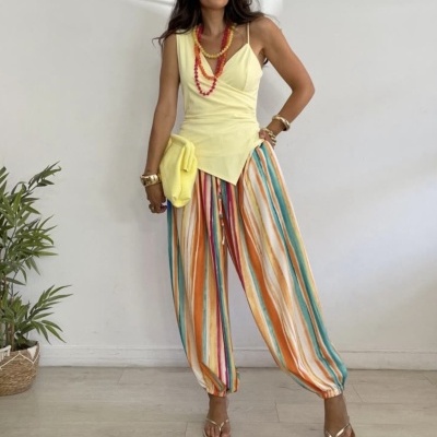 Mulher com blusa amarela, calças riscas multicoloridas e sandálias douradas
