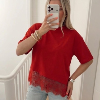 Mulher vestindo t-shirt vermelha com renda e jeans azuis claros com pérolas em selfie