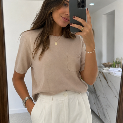 Mulher com t-shirt bege e calças brancas a tirar selfie em espelho