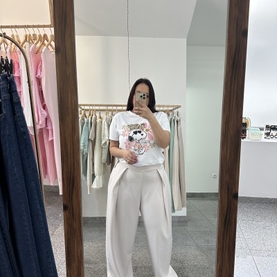 Pessoa no espelho vestindo t-shirt branca com Snoopy e calças largas bege em loja de roupas.