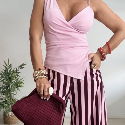 mulher com blusa rosa claro e calças riscas verticais rosa e bordô segurando bolsa bordô