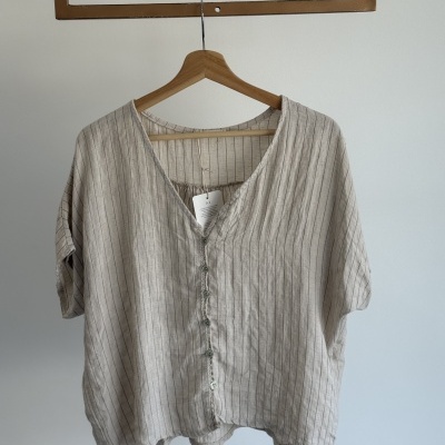 Blusa bege claro com riscas finas pretas em cabide de madeira sobre fundo branco