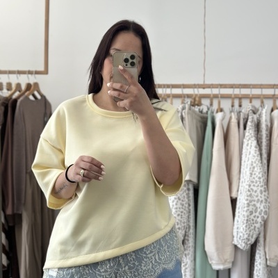 Pessoa com camisola amarela clara de manga larga com renda branca por baixo e jeans azuis claros em loja de roupa.