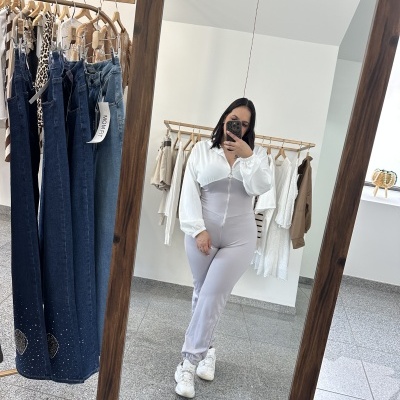 Mulher veste jumpsuit cinzento e branco com ténis brancos refletida em espelho de madeira em loja de roupa.