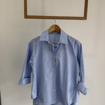 Camisa azul-claro com riscas brancas pendurada em cabide de madeira