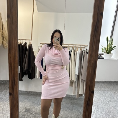 Mulher a usar vestido rosa de malha e botas douradas em frente a espelho de moldura de madeira