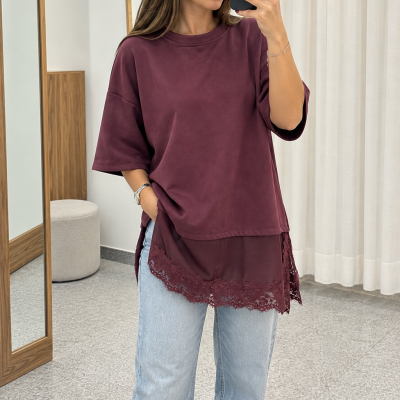Mulher a vestir camisola bordô com renda na parte inferior e calças de ganga claras, tirando selfie em sala com cortinas brancas e espelho de madeira.