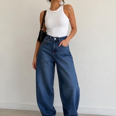 Mulher com top branco, jeans largo azul e sapatilhas brancas, mala preta ao ombro