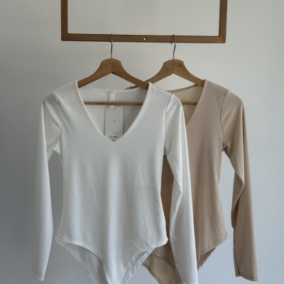 Duas peças de roupa tipo body branco e bege penduradas em cabides de madeira